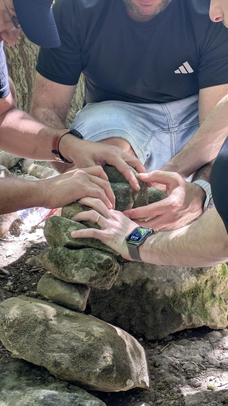 ידיים של חברי הקבוצה בונות יחד ערימת אבנים מאוזנת